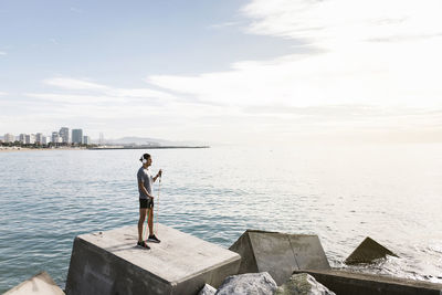 Sportsman pulling resistance band while standing on rock by sea