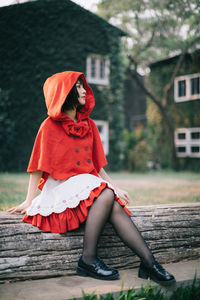 Full length of young woman sitting on log against house