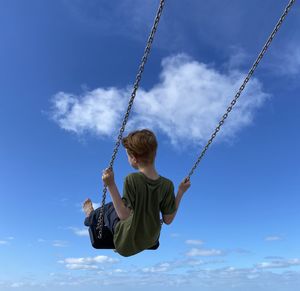 Low angle view of boy swinging against sky