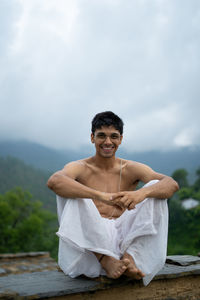 Full length of shirtless young man sitting outdoors