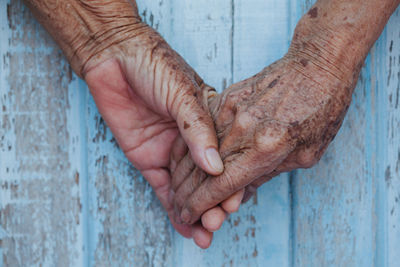 Cropped hands of senior couple holding hands against wall