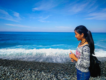 Young woman standing on beach against sky