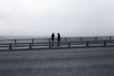 Male friends standing on promenade by sea during foggy weather