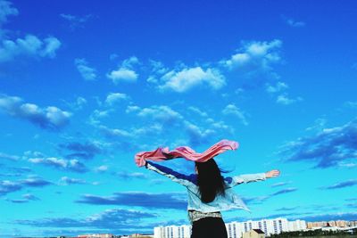 Rear view of woman with arms outstretched standing against blue sky