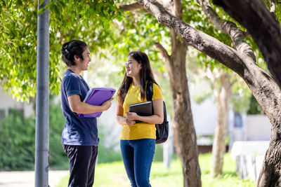 A couple of thai high school students smile while going through the woods with a book in their hands