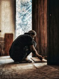 Side view of man sitting on wooden floor