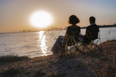 Rear view of people sitting at beach during sunset