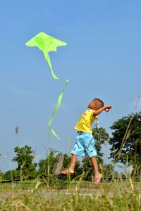 Full length of boy flying kite on field against blue sky