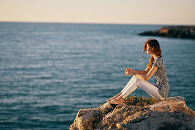 Woman sitting on rock by sea against sky