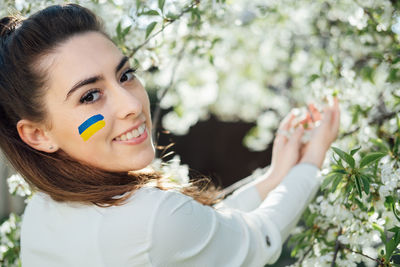 Outdoor portrait of ukrainian woman with blue and yellow ukrainian flag on her cheek on cherry