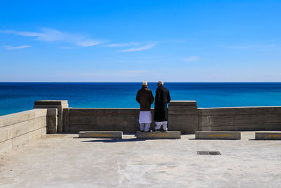 View of men standing on lake shore against blue sky