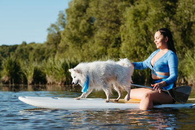 Young woman paddleboarding with her pet on the lake, snow-white dog breed japanese spitz