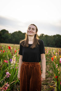 Portrait of smiling young woman standing by flowering plants against sky