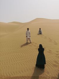 Friends on sand against sky