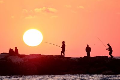 Silhouette men on pier against orange sky