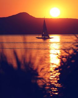 Silhouette sailboat in sea against orange sky