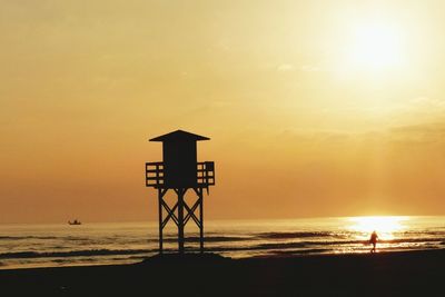 Silhouette lifeguard hut on beach against sky during sunset