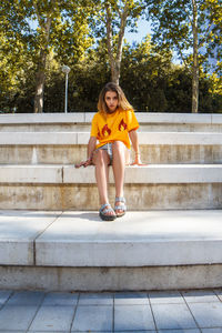 Full length of young woman sitting on steps against trees