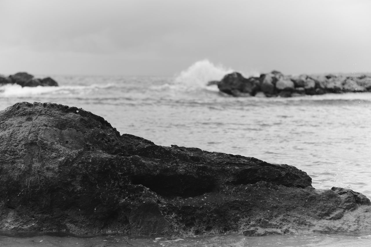 sea, water, rock, black and white, land, wave, beach, shore, coast, wind wave, ocean, monochrome photography, sky, beauty in nature, monochrome, scenics - nature, nature, no people, motion, horizon, environment, tranquility, outdoors, cloud, rock formation, day, coastline, body of water, tranquil scene, travel destinations, sports, horizon over water, sand