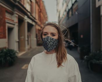 Portrait of beautiful woman wearing mask standing on street in city