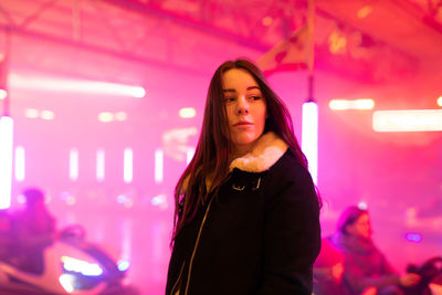 Portrait of young woman standing against illuminated wall