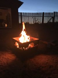 Fire burning on wood against sky at night