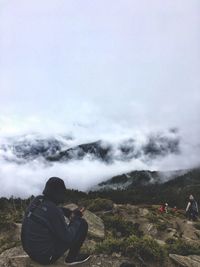 Hiker sitting on mountain during foggy weather