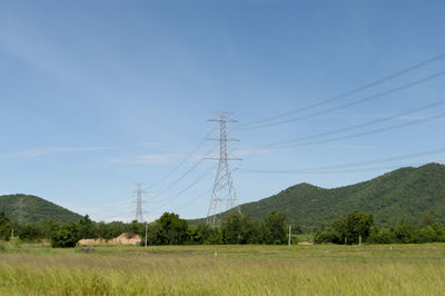 Grassy field by electricity pylons against sky