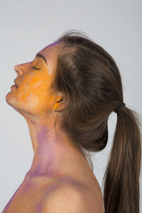 Side view of young woman with painted face dreaming against gray background