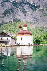 Built structure by lake and buildings against mountain