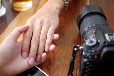 Cropped image of couple holding hands by camera on table