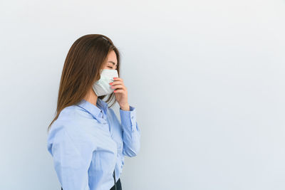 Young woman drinking glass against white background