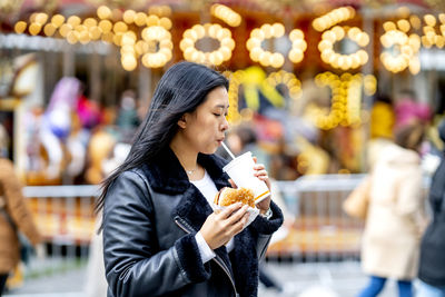 Woman holding burger and drinking from disposable cup at park