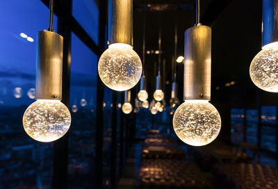 Low angle view of illuminated lighting equipment hanging at night