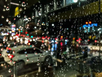 Cars on illuminated road seen through wet window