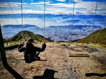 Rear view of woman sitting swing at mountain against sky