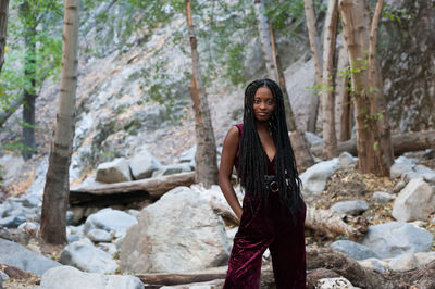 Portrait of woman with long braided hair standing on rock in forest