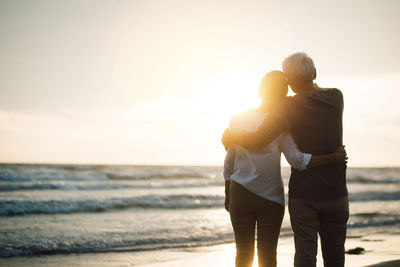 Couple standing on beach against sky during sunset