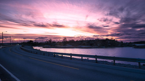 Road by city against sky during sunset