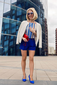 Young business woman in short blue trunks standing and waiting for a meetingfrom the bank of glass 