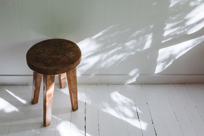 Wooden stool near the white wall, rustic interior details. natural morning light.