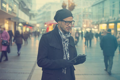 Man wearing warm clothing using digital tablet in city