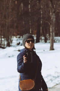 Mature woman holding mobile phone while standing by snow covered field