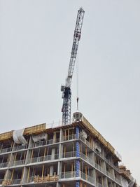 Low angle view of crane on buildings against clear sky