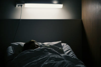 Man sleeping on bed in illuminated bedroom