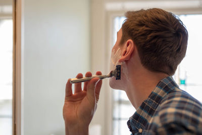 Close-up of young man shaving at home