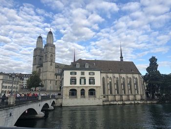 View of buildings by river against cloudy sky