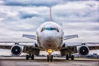 Airplane on airport runway against cloudy sky