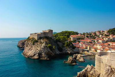 Buildings by sea against clear blue sky