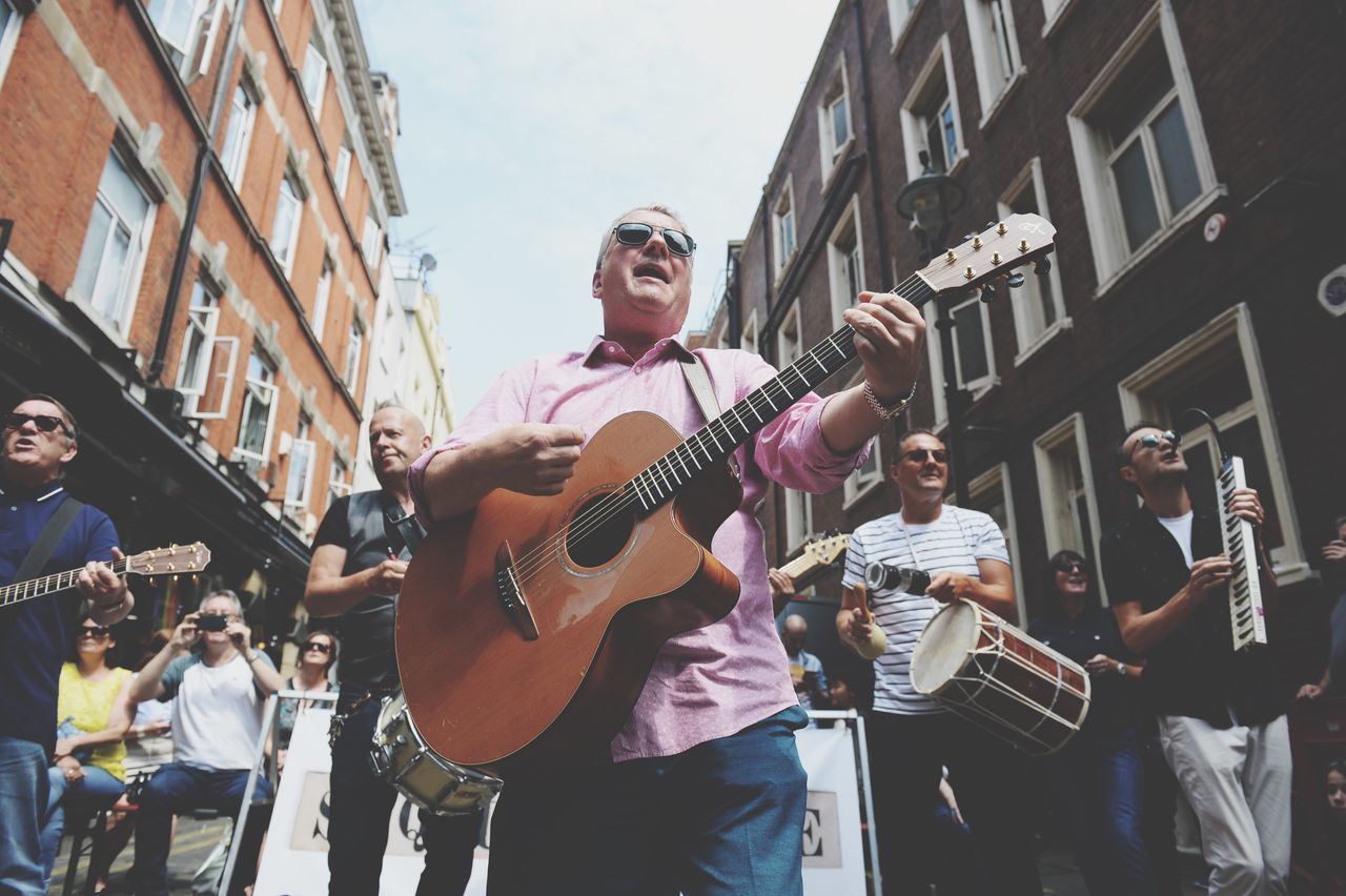 musical instrument, music, guitar, string instrument, musical equipment, city, artist, architecture, building exterior, musician, performance, group of people, arts culture and entertainment, playing, built structure, men, real people, street performer, street musician, day, skill, acoustic guitar, plucking an instrument, outdoors